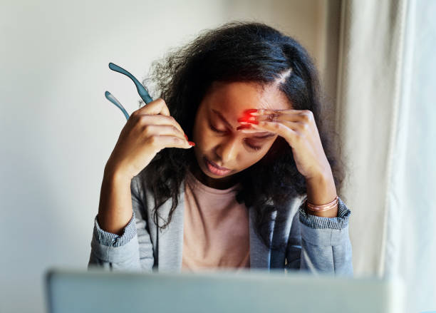 Shot of a young woman suffering from a headache while using a laptop at home